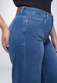 Blauwe denim jeans met een getailleerd ontwerp, voorzien van een middelhoge taille, vijf zakken en een leren label op de achterzijde van de tailleband.