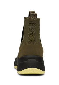 Botas de tobillo de tela verde con un fondo texturizado, que cuentan con paneles laterales elásticos y una suela de goma negra con un acento amarillo.