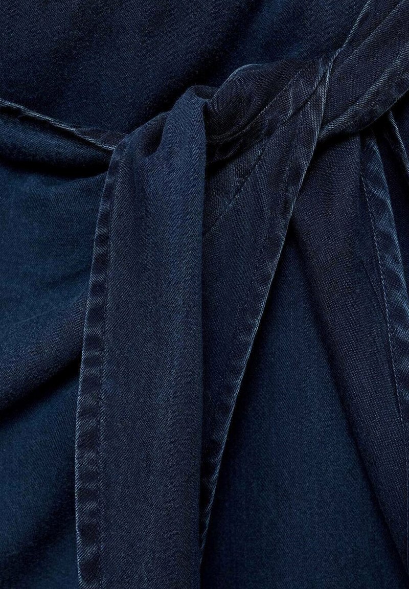 Tissu bleu foncé avec une texture lisse, présentant un détail de taille nouée et un design fluide. Pas de motifs visibles ni de quincaillerie.