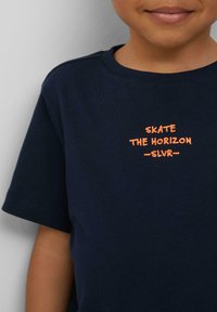 Navyblauwe katoenen t-shirt met oranje bedrukte tekst: "SKATE THE HORIZON -SLVR-." Ronde halslijn en korte mouwen.