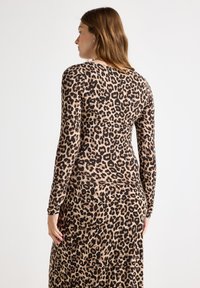 Leopardmönstrad långärmad klänning i tan och svart, med en figurnära design och slät textur, rund halsringning och helärmade ärmar.