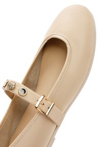 Bailarina de cuero beige con punta redondeada, correa en el tobillo con herrajes en tono dorado y acentos circulares, y un forro interior suave.