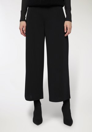 Pantaloni neri a gamba larga realizzati in tessuto liscio, con vita alta e lunghezza cropped, abbinati a stivali neri con punta a punta.