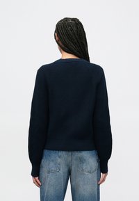 Μπλε πουλόβερ πλεκτό με στρογγυλή λαιμόκοψη, ριμπ μανσέτες και τελείωμα. Διαθέτει υφή με ανάγλυφο μοτίβο και εφαρμοστή σιλουέτα, συνδυασμένο με ανοιχτό μπλε τζιν.
