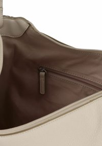 Beige leren handtasje interieur met een gladde textuur, voorzien van een klein met rits afgesloten vak en een satijnen voering in een lichter tint.