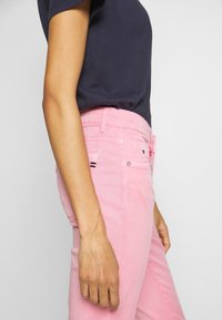 Jean en coton rose avec poches latérales, taille médiane et silhouette ajustée. Accentué par un petit logo et des détails de couture contrastés.