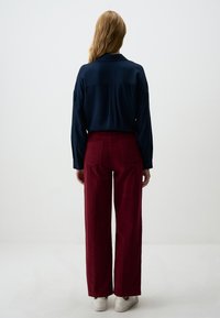 Marineblauw overhemd met lange mouwen en bordeauxrode hoge taille wijde broek, gecombineerd met witte sneakers. Glad materiaal met borstzakken en een getailleerde pasvorm.