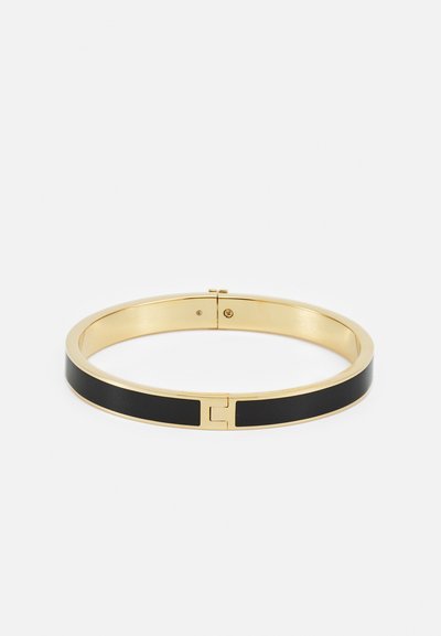 Zlatý náramok v tvare bangles s čiernou emailovou pruhou, hladkým povrchom, okrúhlym tvarom a uzáverom s malým emblémovým detailom.