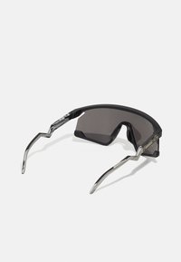 Sportsonnenbrille mit einem schwarzen Kunststoffrahmen, dunklen Gläsern und metallischen Akzenten. Verfügt über ein kantiges Design und schlanke, geschwungene Bügel.
