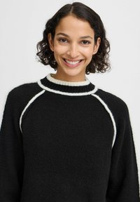 Maglione nero con strisce accentuate bianche lungo il colletto e le cuciture delle spalle. Realizzato in un materiale a maglia morbido e testurizzato.