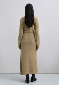 Rochie lungă tricotată dintr-un material bej texturat, având mâneci lungi și o talie ușor ajustată. Pură cu botine negre cu toc.