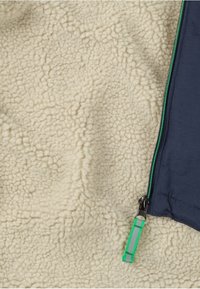 Fleece-jacka med en krämfärgad, texturerad insida och en marinblå utsida. Grön dragkedja med en mönstrad dragflik.