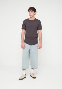 Μαύρο γκρι μπλουζάκι με στρογγυλή λαιμόκοψη σε συνδυασμό με ανοιχτό μπλε τζιν σορτς με φαρδιά πόδια. Τα σορτς έχουν ξεφτισμένο τελείωμα και φοριούνται με λευκές ριγέ κάλτσες και μπεζ αθλητικά παπούτσια.