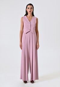 Violetter Jumpsuit mit einem figurbetonten Oberteil und weiten Hosenbeinen, versehen mit Knopfakzenten und einer glatten, fließenden Stofftextur.