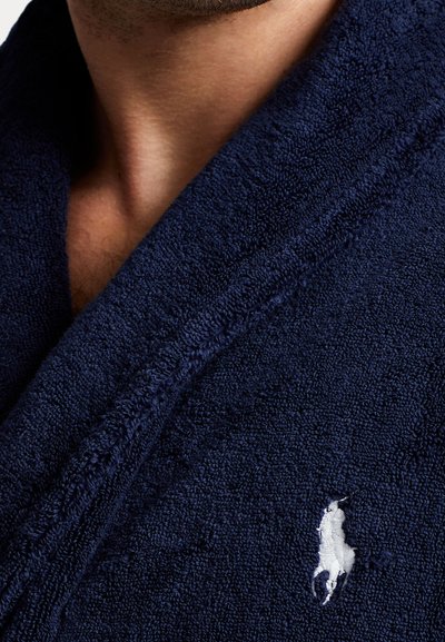Bata de baño de felpa en color azul marino con una textura suave y cuello tipo chal, que presenta un logo bordado en blanco en la parte frontal.