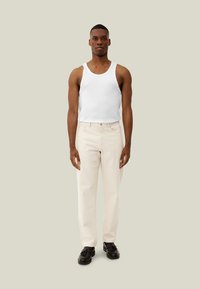 Camiseta sin mangas blanca, pantalones rectos de mezclilla beige claro y zapatos negros. Diseño simple con una textura suave y colores neutros.