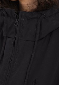 Giacca nera con zip, dotata di cappuccio, cordini regolabili e una texture morbida. Dettagli di cucitura discreti sul davanti.