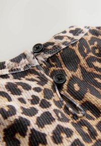 Leopardenmusterstoff mit gerippter Textur, ausgestattet mit zwei schwarzen Knöpfen am Ausschnitt und kontrastierenden Nahtdetails.