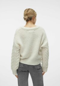 Un pull en tricot épais avec des manches en tricot torsadé, un large col et un ourlet côtelé ; associé à un pantalon en denim gris.