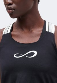 Gros plan d'une personne portant un débardeur noir avec un symbole infini blanc et des bretelles d'épaule blanches rayées.