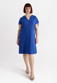 Niebieska sukienka krótki rękaw z dekoltem w serek i wiązaniami przy rękawach, cechująca się luźnym krojem i gładkim materiałem zapewniającym komfort noszenia.
