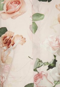 Zacht roze stof met een patroon van grote, delicate rozen in tinten roze en perzik, vergezeld van groene bladeren.