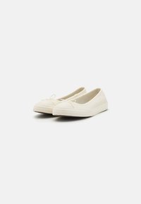Ballerine di tela bianca con punta arrotondata, suola in gomma texturizzata e dettaglio a fiocco decorativo sulla parte anteriore. Design semplice e a profilo basso.