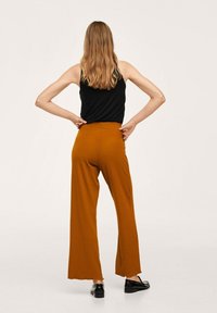 Débardeur noir associé à un pantalon orange côtelé, taille haute, jambes larges, avec un ourlet brut, porté avec des chaussures noires, vue de dos.