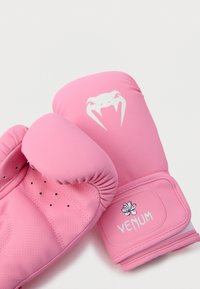 Ružičaste boksačke rukavice s podstavljenim palčevima, perforiranom teksturom, logotipom Venum i cvjetnim ukrasom. Izrađene od sintetskog materijala, dizajnirane za trening.