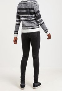 Jean ajustado negro combinado con un suéter de rayas grises y blancas con un patrón texturizado. Zapatos negros con suelas blancas completan el look.