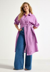 Lilla stribet skjortekjole med korte puffede ærmer og bindebånd i taljen. Kombineret med blå denimbukser med vide ben. Glat tekstur, lukning med knapper.