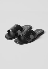 Sandales plates noires à enfiler avec larges brides cloutées et orteils ouverts, taille 37, positionnées sur un fond blanc.