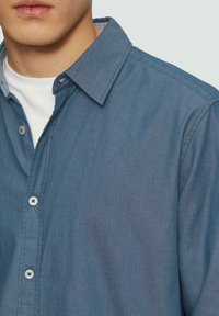 Chemise boutonnée texturée bleu clair avec un col, présentant un motif à rayures subtil et des boutons blancs contrastants.