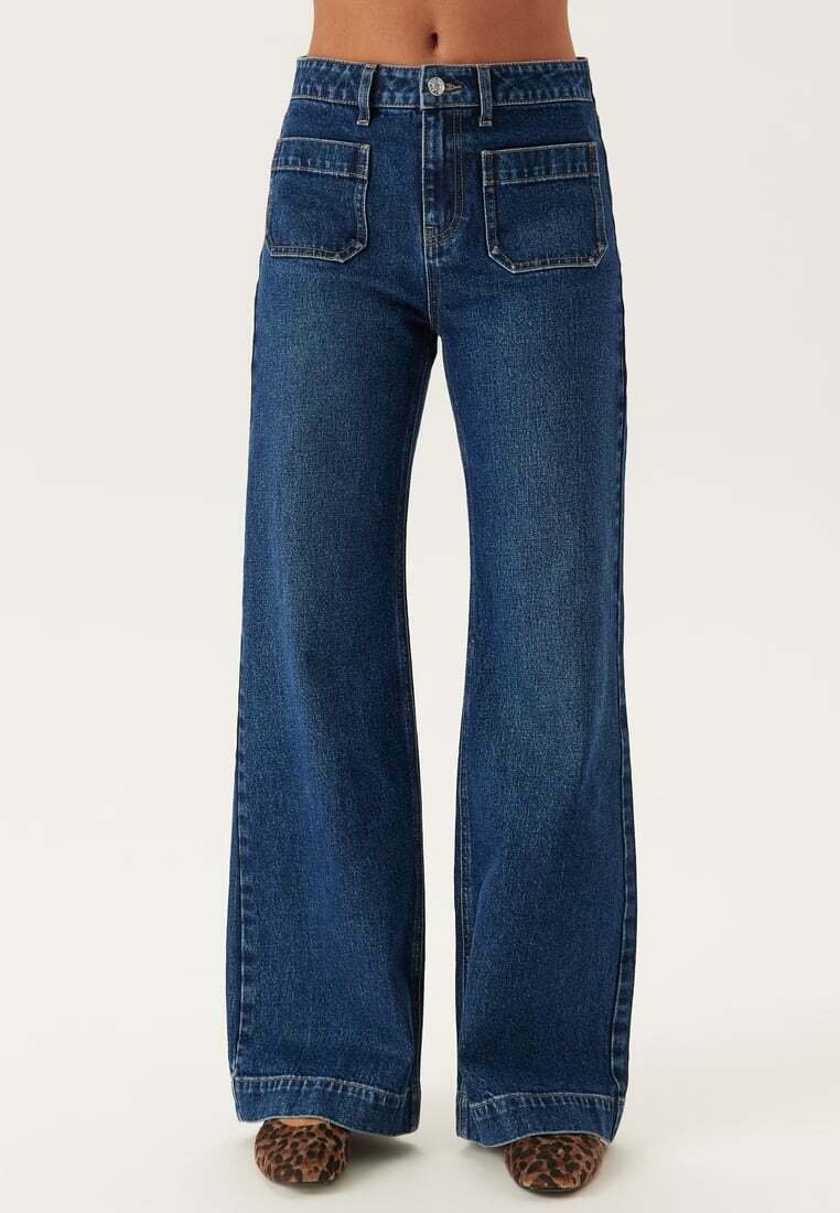 Mörkblå denimjeans med vida ben som har hög midja, fyra fickor och en klassisk knapp- och dragkedjestängning. Strukturerad tyg med en slät yta.