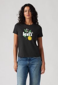 Černé bavlněné tričko s grafickým designem, na kterém je citron, listy a květiny, s textem "levi's" v světle zelené barvě. Krátké rukávy a uvolněný střih.