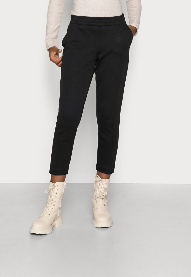 Černé zúžené tepláky s jemnou texturou a elastickým pasem, doplněné světle barevnými šněrovacími bojovými botami.