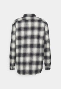 Chemise en flanelle à manches longues présentant un motif à carreaux noir et blanc, avec un col et des poignets boutonnés, confectionnée dans un tissu texturé.