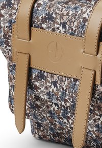 Brun blommönstrad tygväska med läderdetaljer, med två robusta remmar och en märkt läderplatta.