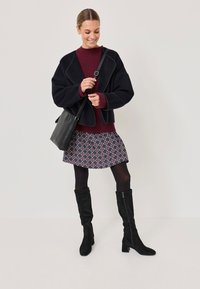 Black cropped jacket with a soft texture and contrasting seams, maroon ribbed sweater, floral patterned skirt, and knee-high black suede boots.
