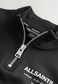 Melnā sporta jaka ar augstu apkakli, kas aprīkota ar sudraba rāvējslēdzēju un "ALLSAINTS" logo. Izgatavota no mīksta materiāla ar teksturētu apdari.