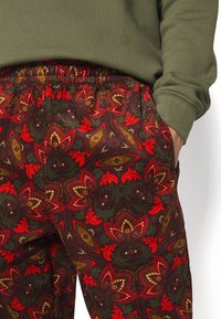 Blommönstrade kordfløyelsbyxor med röda, gröna och gyllene nyanser samt resårmidja. Materialet är ribbat och mjukt.