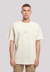 Beige oversized cotton t-shirt with short sleeves, featuring printed text in Japanese and a star accent on the front.