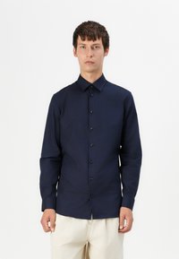 Camisa de botones de manga larga en azul marino, confeccionada en tejido suave, con un cuello clásico y botones negros en la parte delantera.