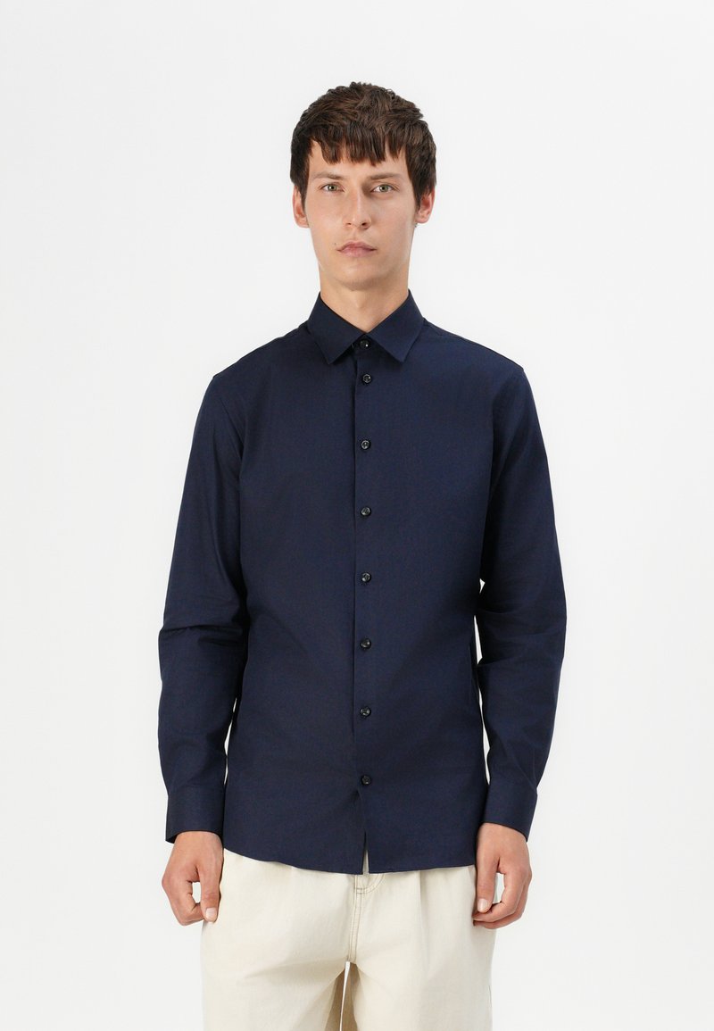 Camisa de botones de manga larga en azul marino, confeccionada en tejido suave, con un cuello clásico y botones negros en la parte delantera.