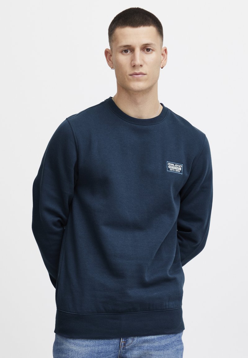 Marineblauwe sweatshirt van een zachte katoenen mix, met een ronde hals, ribbelmanchetten en een klein wit logopatch op de borst.