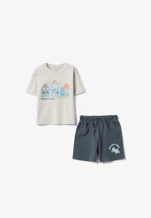 Camisa beige de manga corta con dibujos de skaters caricaturescos y texto "Project Ride", combinada con pantalones cortos de color gris oscuro con cordón y gráfico de skate.