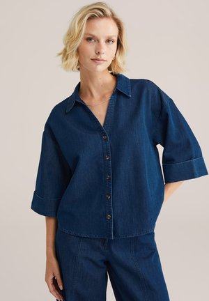 Denim button-up shirt in dark blue, featuring a collar, short sleeves, and brown buttons along the front, with a relaxed fit and smooth texture.
