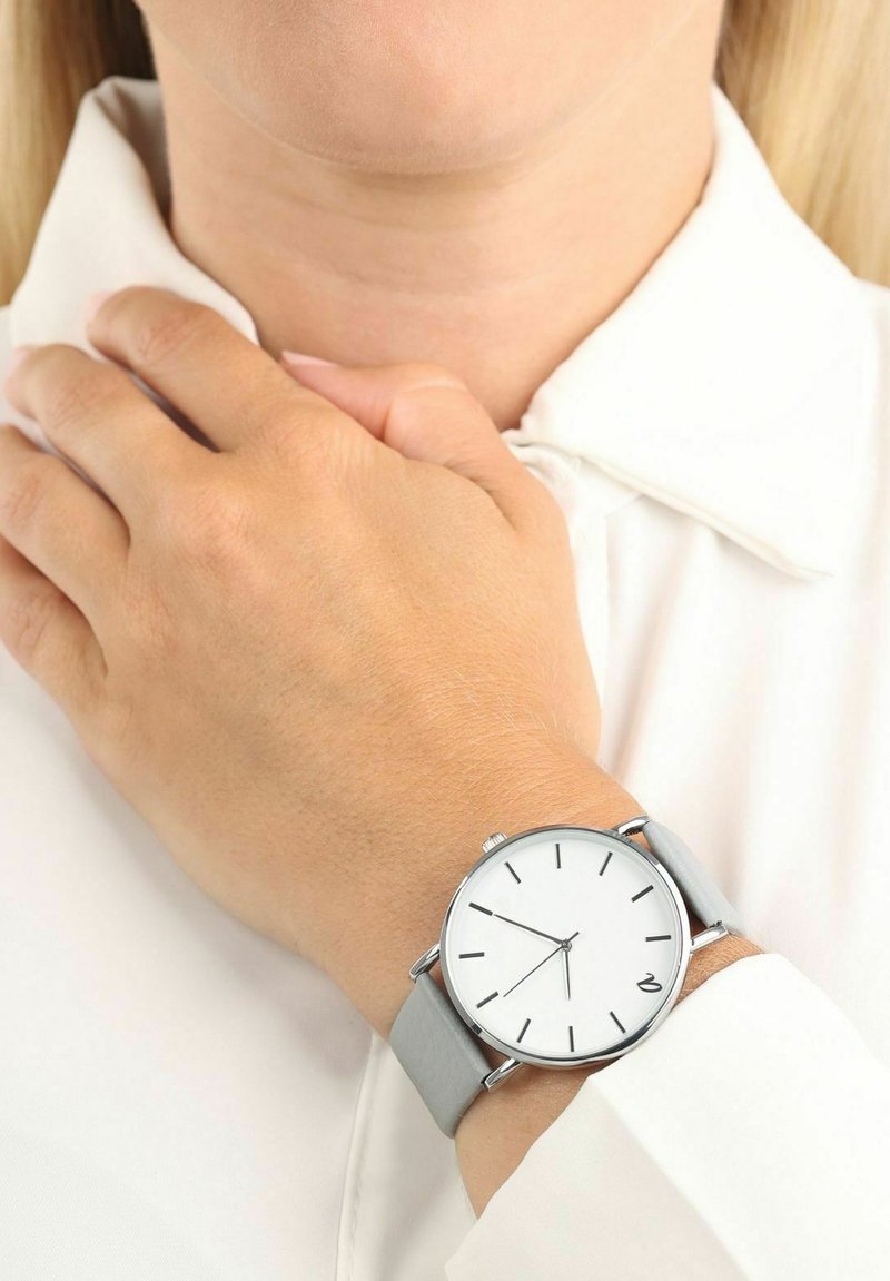 Silberne Uhr mit weißem Ziffernblatt und schwarzen Stundenmarkierungen, ausgestattet mit einem hellgrauen Lederarmband und einem runden Gehäuse aus Edelstahl.