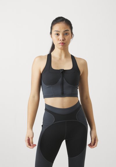 Il reggiseno sportivo nero e grigio presenta una zip frontale, spalline larghe e pannelli. Leggings a vita alta con aperture curve e dettagli a contrasto.