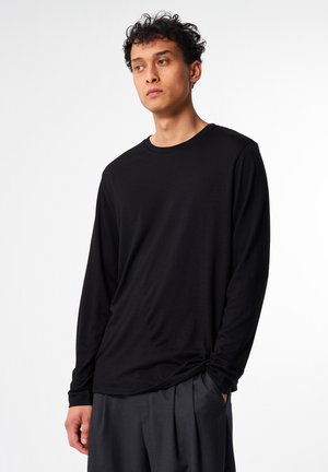 Schwarzes Langarmshirt aus weichem Stoff mit Rundhalsausschnitt und lockerer Passform. Kombiniert mit lockeren grauen Hosen. Minimalistisches Design.